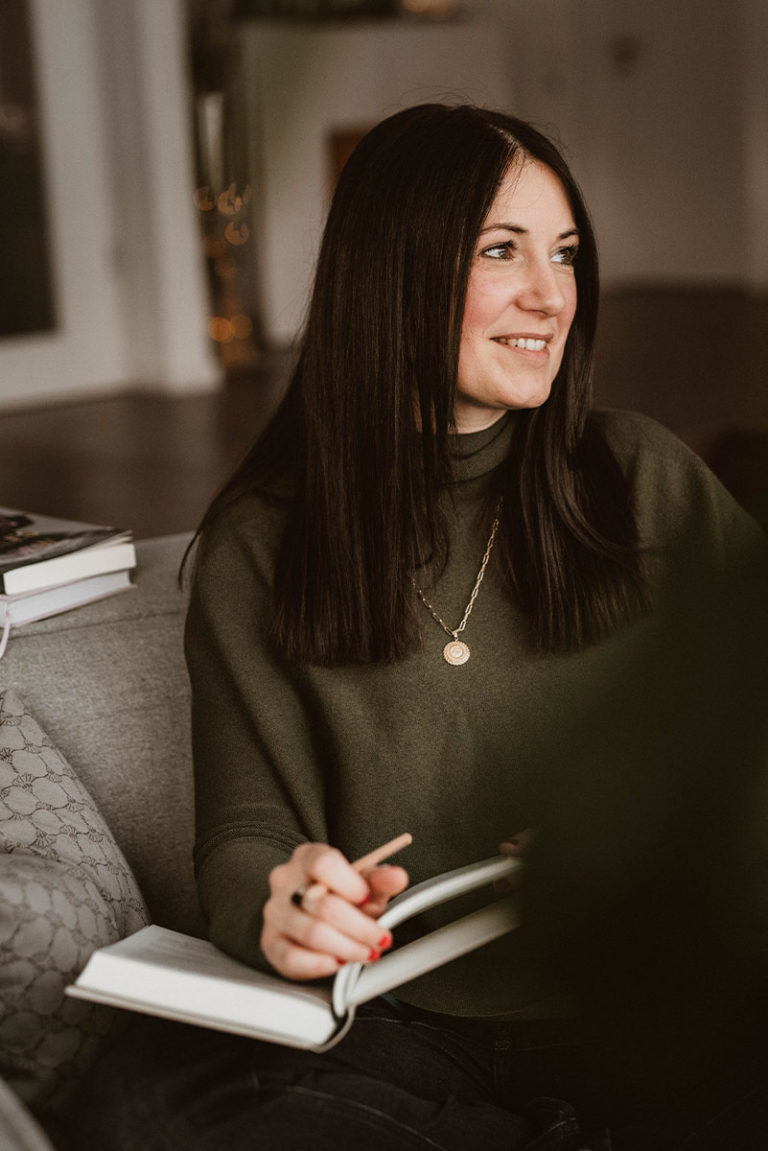 Johanna sitzt mit ihrem Buch auf einem Wohnzimmer Sesssel bei sich zuhause in Ehingen bei Ulm, sie lächelt richtung fenster und ihr blick wandert weg von der kamera