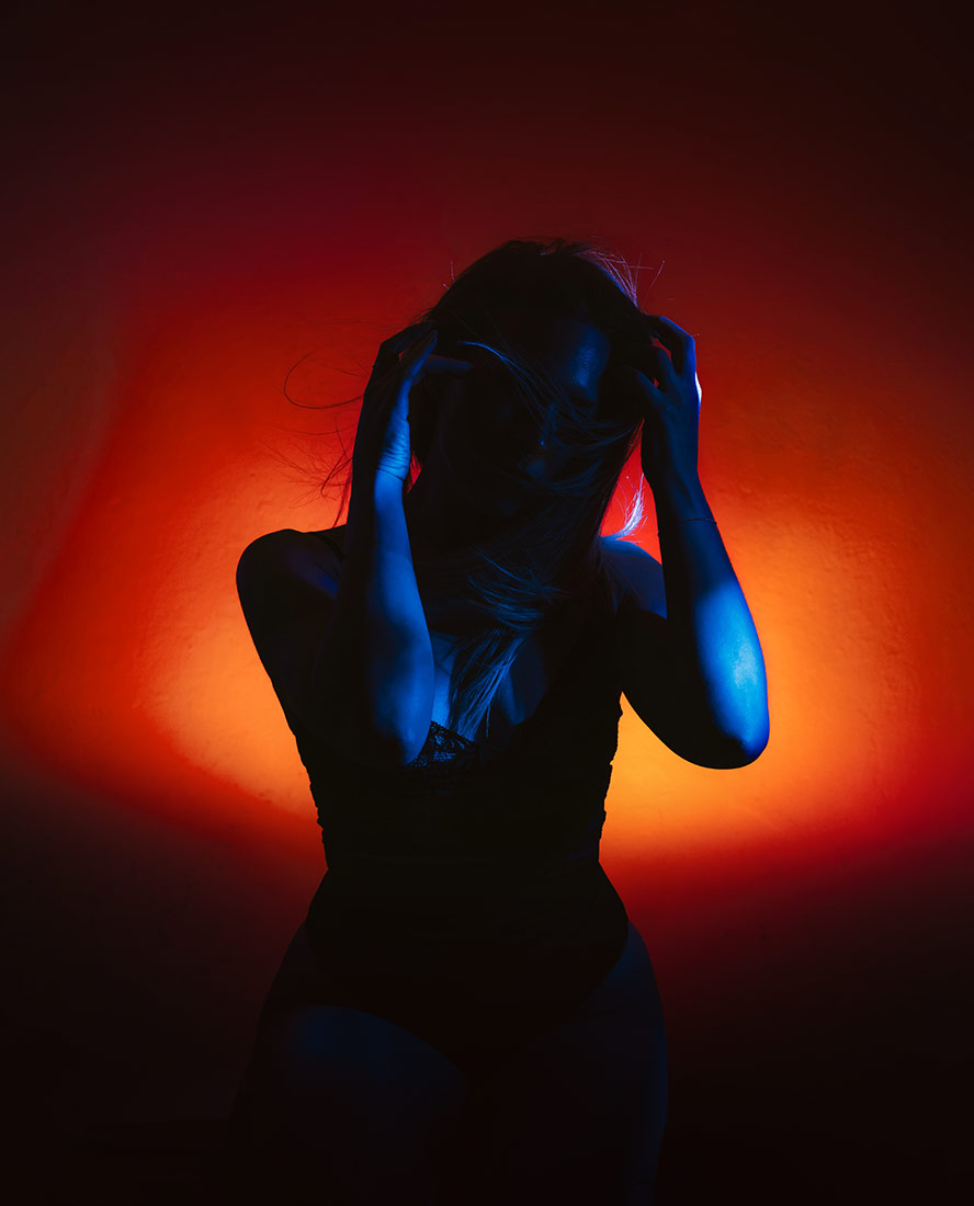 Dramatic self portrait with red and blue complementary lighting, hands in hair and deep shadow contrast