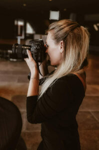 Sabine hält lächelnd eine Kamera vor das Gesicht während eines Fotoshootings