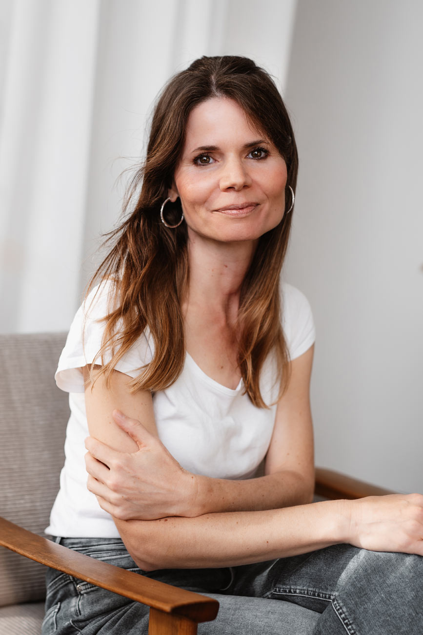 Personal Branding Portrait einer Beraterin im Bereich Entspannungspädagogik in natürlichem Licht sitzend auf einem Holzstuhl