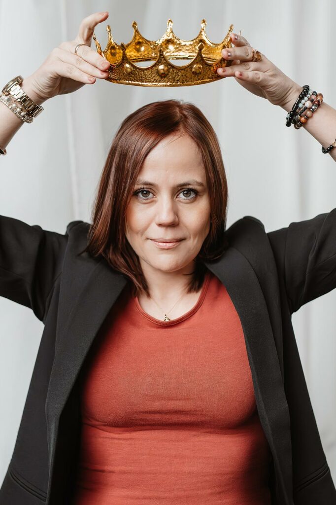 Personal Branding Portrait einer Frau mit rotem Oberteil, die eine Krone über ihren Kopf hält